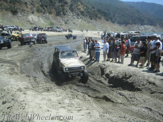 1987 Suzuki Samurai navigating a muddy off-road course with spectators watching