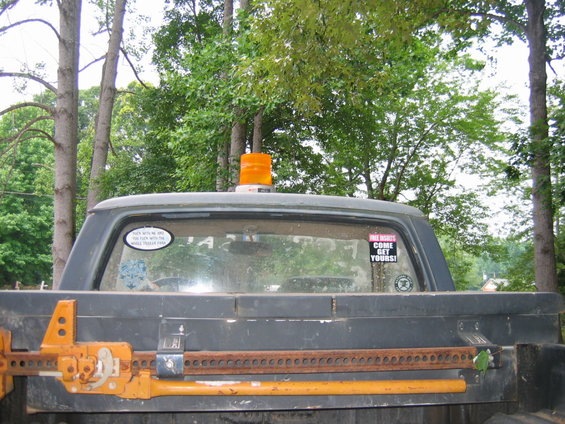 Back of a dark-colored pickup truck with an orange light on top. Two stickers are on the rear window