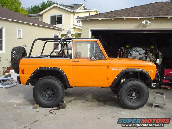 Orange 1977 Ford Bronco with roll cage and spare tire on rear