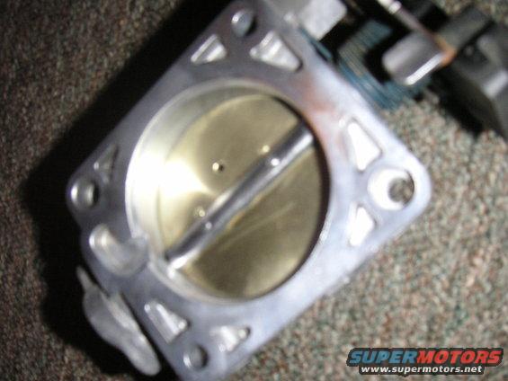 Throttle body with a metal butterfly valve inside, resting on a carpeted surface