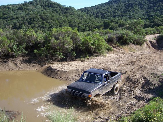 Dark pickup truck splashing through muddy water on a dirt track