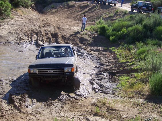 Ford F-series truck going through mud. Another Bronco is visible on the hill