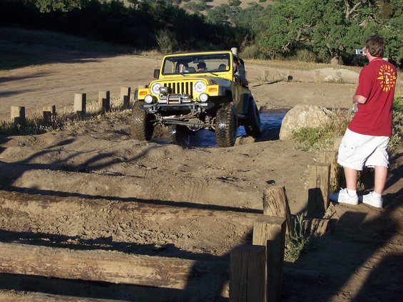 Yellow Jeep Wrangler navigating an off-road obstacle course, front view