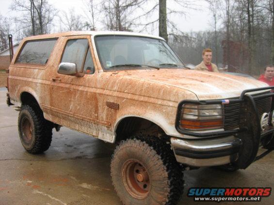 Mud-covered white 1992 Ford Bronco with aftermarket bull bar and large tires, parked on a wet surface