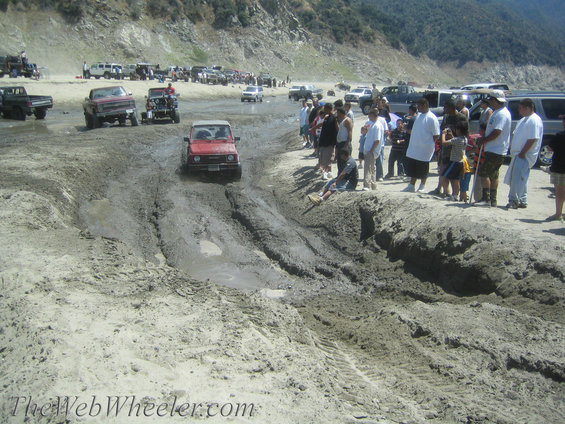 Red 1987 Suzuki Samurai navigating a muddy track with spectators watching