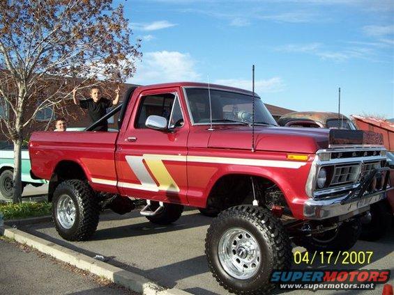 Red lifted Ford F-250 pickup truck with chrome wheels and side decals, parked outdoors