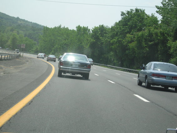 Dark sedan from rear on highway, reflecting sun. Appears to be a 1990s model