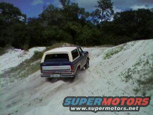 Dark blue and white Ford Bronco driving up a sandy hill