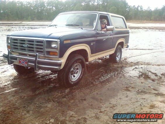 Blue Ford Bronco with tan trim driving off-road in muddy terrain