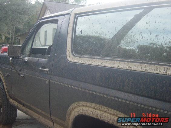 Mud-covered dark blue Ford Bronco with a tan top, seen from the side