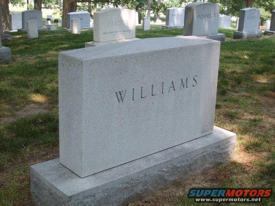 Tombstone with 'WILLIAMS' engraved on it, set in a grassy cemetery with other headstones visible