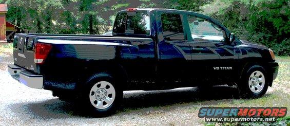 Black 2007 Nissan Titan pickup truck, side view, parked on gravel with trees and a building in the background