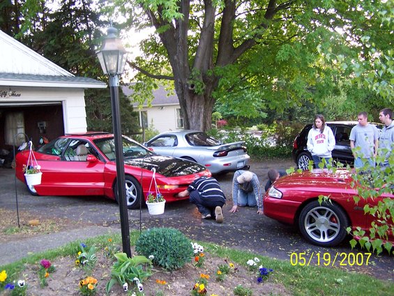 Red 1996 Ford Probe with hood open, silver Mazda RX-7, and black SUV parked in driveway with people around