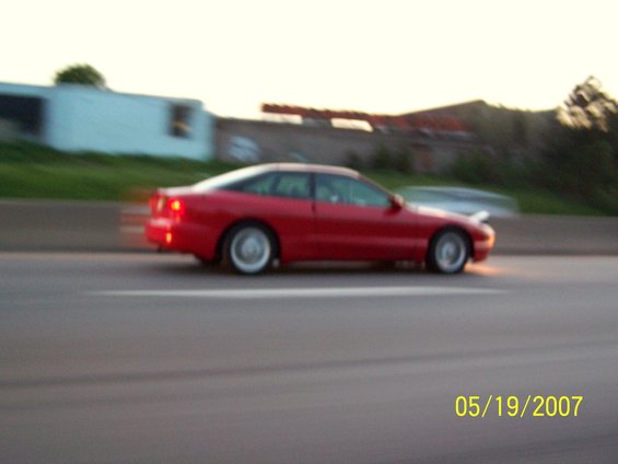 Red coupe driving on highway, date stamp 05/19/2007