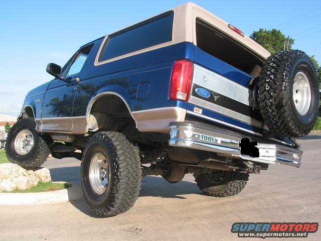 Blue 1996 Ford Bronco with tan top, lifted with large tires, spare tire mounted on rear door