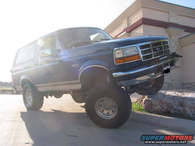 1996 Ford Bronco with aftermarket wheels and tires, lifted suspension, driving over a curb and rock