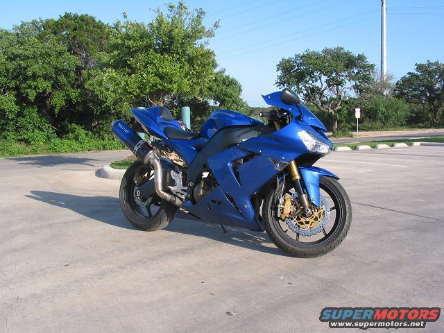 Blue sport motorcycle parked in a lot. It has gold brake calipers and a custom exhaust