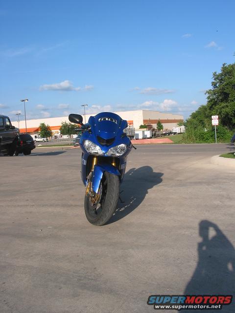 Blue motorcycle parked on concrete, front view. Black truck visible to the left