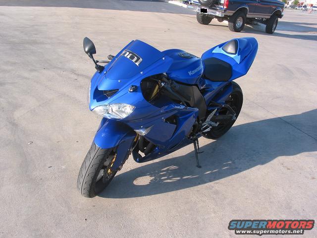 Blue Kawasaki sportbike parked on concrete, with a blue Ford Bronco in the background