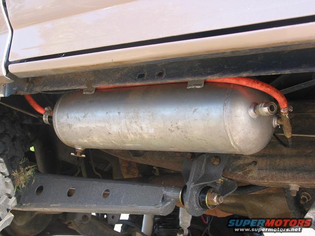 Underside of a vehicle showing an air tank mounted to the frame with an orange hose