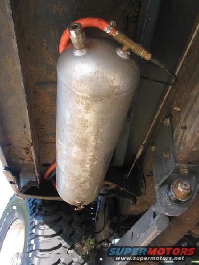 Underside view of an air tank with orange hose and brass fittings, mounted to vehicle frame