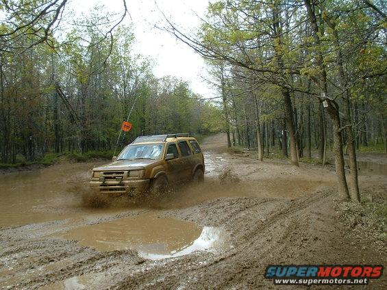 Gold SUV driving through a muddy forest road, splashing water