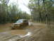 1991 Ford Bronco - A gold SUV navigates a challenging muddy trail, kicking up water as it goes.