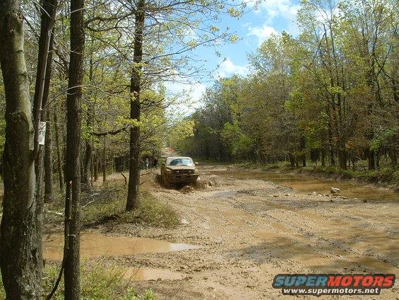 1991 Ford Bronco driving through a muddy forest road