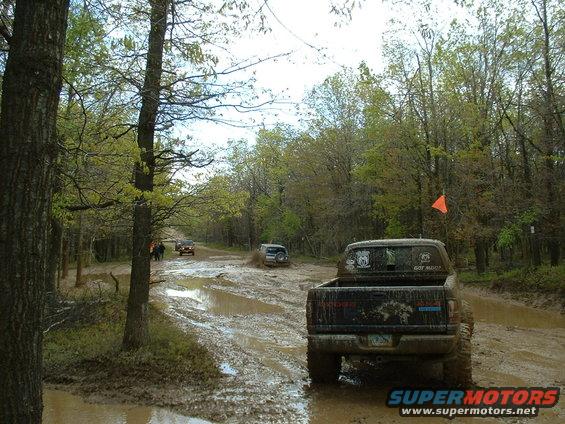 Muddy off-road scene with several trucks and SUVs navigating a trail
