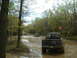1991 Ford Bronco - Multiple off-road vehicles traverse a muddy trail through a wooded area.