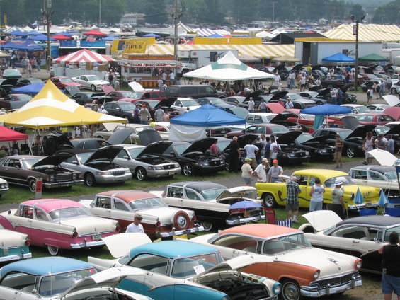 Outdoor car show with numerous vehicles and vendor tents under a bright sky