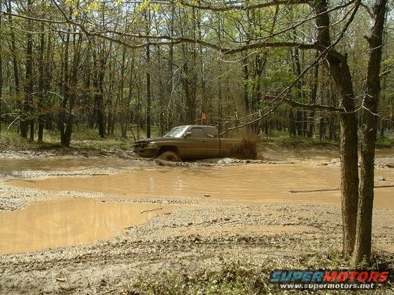 Brown pickup truck splashing through a muddy forest stream