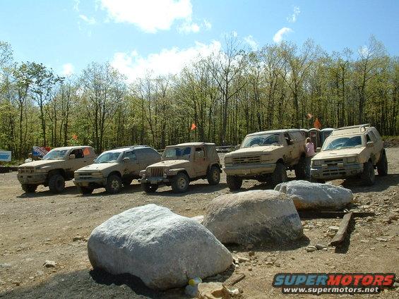 1991 Ford Bronco front grille and headlights, tan color, parked with other off-road vehicles