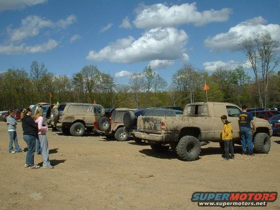 Several off-road vehicles, including a lifted pickup truck and SUVs, parked on a dirt lot under a cloudy sky
