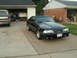 1988 Ford Mustang - A black 1988 Ford Mustang with a prominent hood scoop and aftermarket wheels is parked in a driveway next to a pickup truck.
