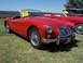 2002 Ford Mustang - A red MGA convertible is parked on grass next to another red car.