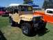 2002 Ford Mustang - A tan Jeep CJ with a white soft top and chrome wheels is parked on grass at an outdoor event.