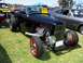 2002 Ford Mustang - A black convertible hot rod with a prominent engine is displayed on a grassy field next to other vehicles.