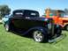 2002 Ford Mustang - A classic black coupe with chrome wheels sits on a grassy field next to an orange truck.