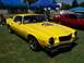 2002 Ford Mustang - A bright yellow 1974 Chevrolet Camaro Rally Sport is displayed outdoors, with a red car visible to its right.