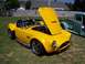 2002 Ford Mustang - A yellow convertible sports car is displayed outdoors with its hood open, parked next to a teal pickup truck.
