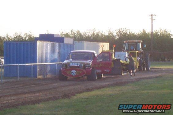 Red pickup truck with 'PDR' logo on front, next to a yellow tractor. Both are on a dirt track