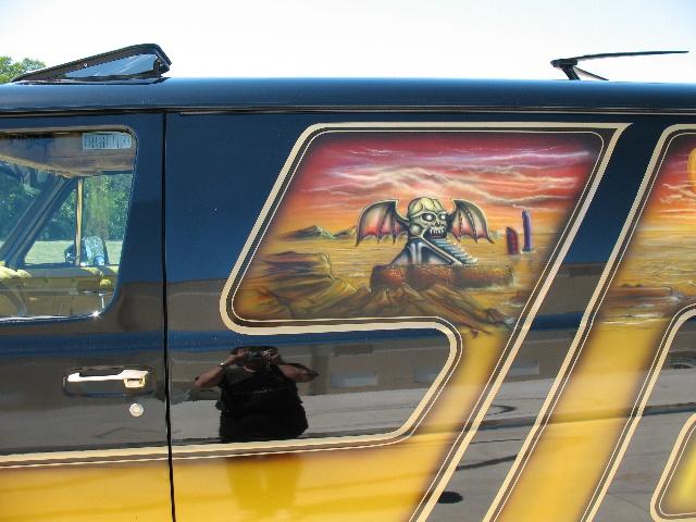 Side of a dark blue and yellow van with custom airbrush art depicting a desert landscape with a winged skull figure