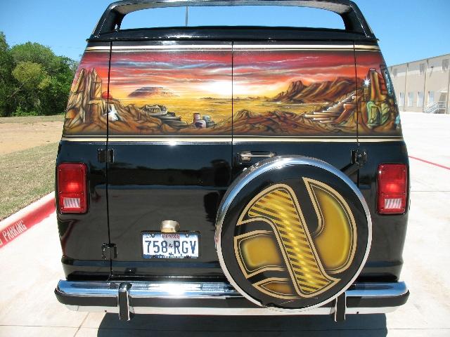 Black van with custom desert landscape mural on the back doors. Has a spare tire cover with a gold and black design