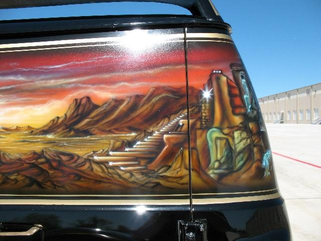 Side of a black van with a desert landscape airbrushed on it, mountains and a staircase