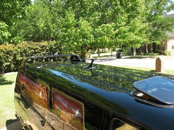 Black van with custom sunset and heart mural painted on the side. Roof rack and sunroof visible
