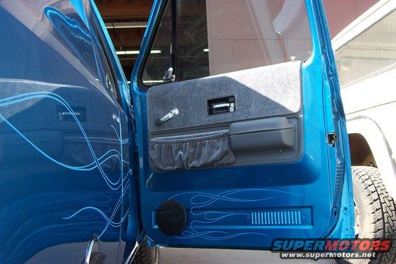 Blue pickup truck door open, showing interior panel with grey fabric and chrome handle. Pinstriping on the exterior door