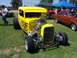 2002 Ford Mustang - A yellow hot rod is displayed on grass with other vehicles and tents in the background.
