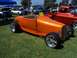 2002 Ford Mustang - An orange hot rod is parked on a grassy field next to a red pickup truck and other vehicles.