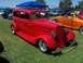 2002 Ford Mustang - A classic red hot rod sedan is parked on a grassy field at an outdoor car show.